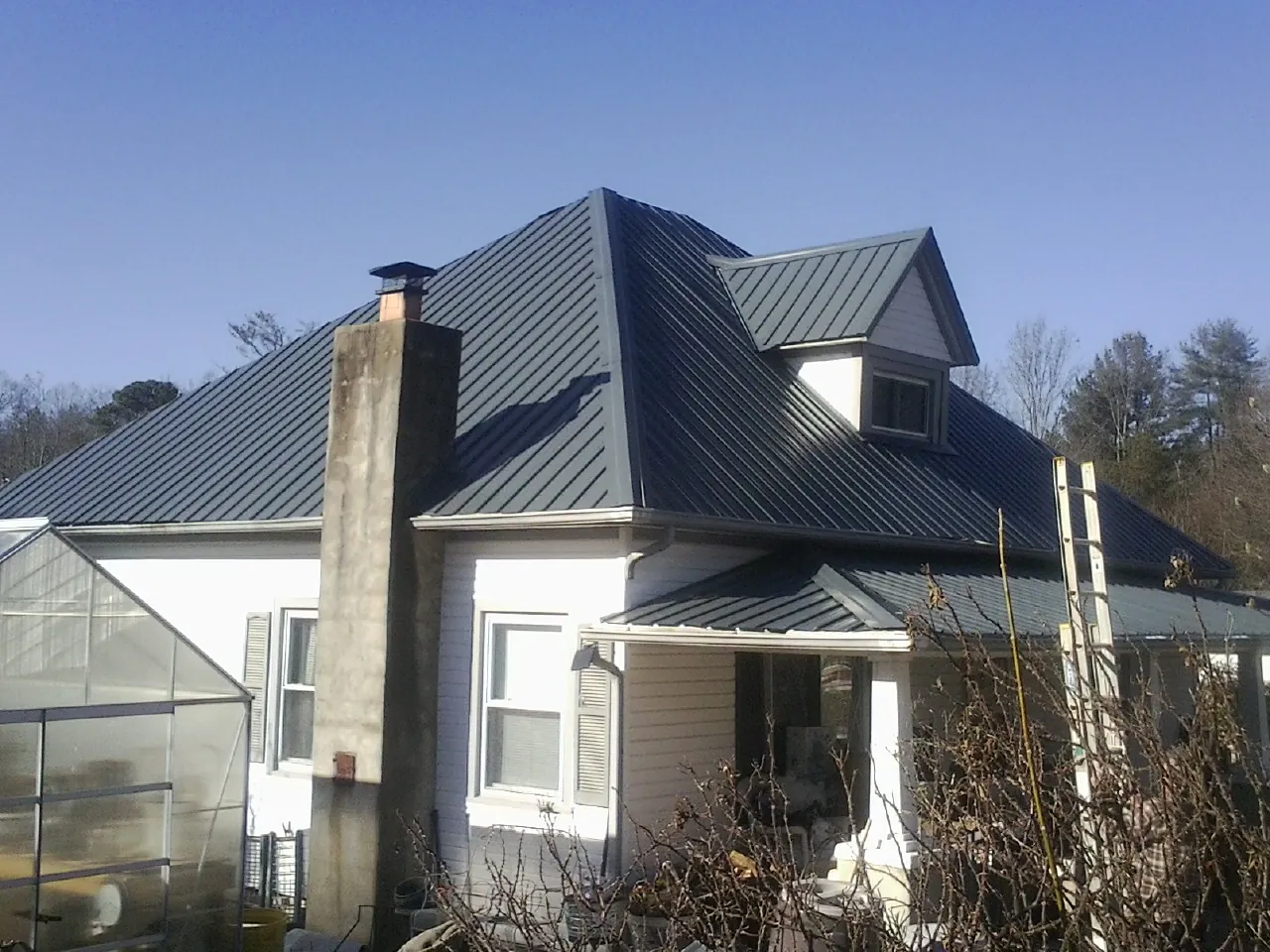Dark blue standing seam metal roof on a white farmhouse with dormer — Slate & Tile Roof Repair by Roofing Brothers in Johnstown