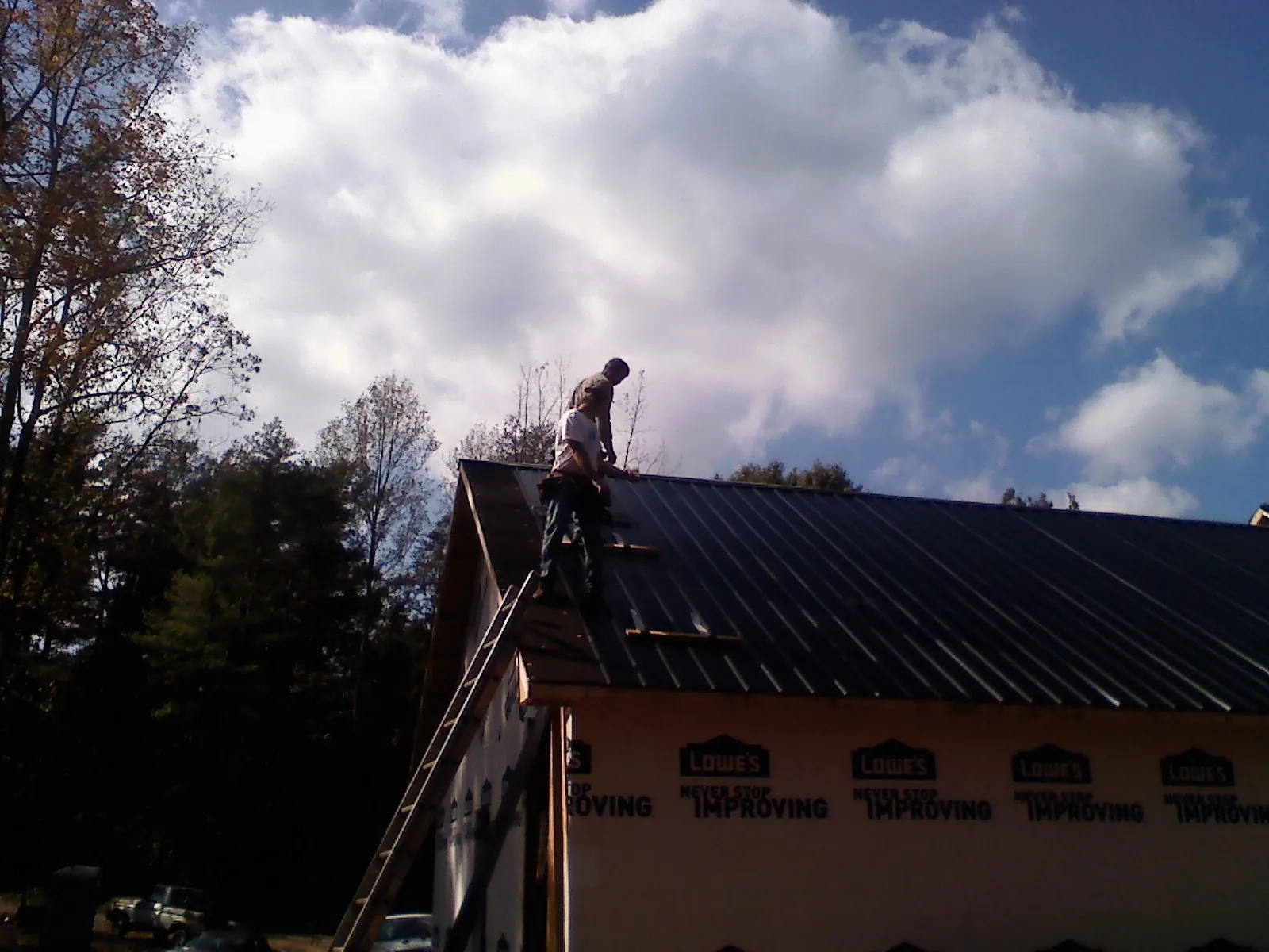 Roofer fastening dark metal panels high against a cloudy sky, from a Roof Inspection job in Johnstown